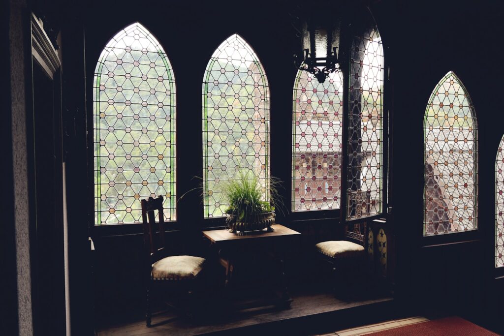 Intérieur de style médiéval : baies en arc en ogive, vitraux, boiseries sombres et lustre en fer forgé